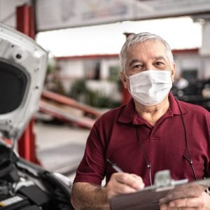 Portrait of auto mechanic senior man with face mask at auto repair shop