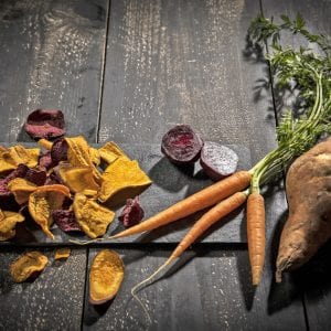 Vegetable chips made of carrots, sweet patatoes and beetroot on dark wood