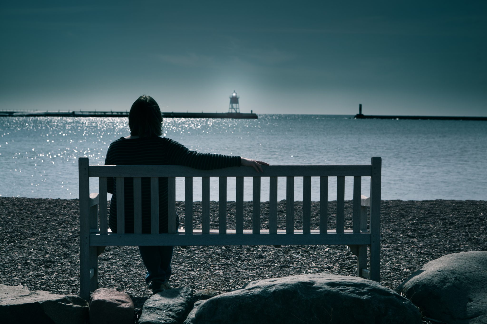 Lady sitting on a bench looking at a lighthouse