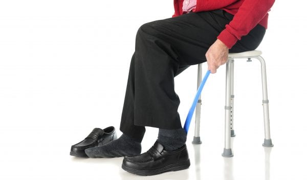 Close-up view of a senior man sliding into his loafers with the aid of a long-handled shoe horn. On a white background.