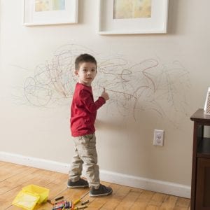 Mixed Race boy drawing on wall with crayons