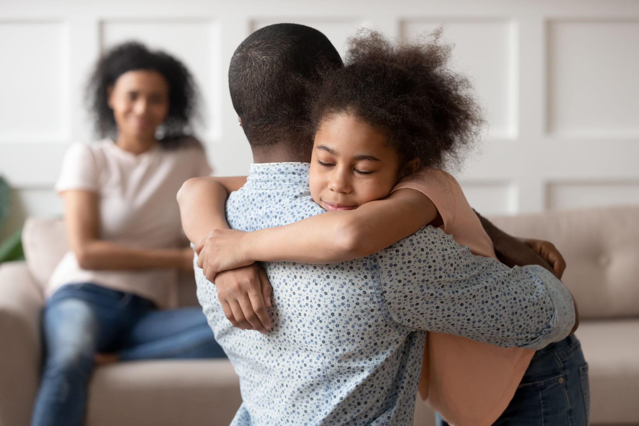 Managing family conflicts;Young african american man holding, embracing, comforting smiling happy calm black cute kid daughter, blurred mother sitting on couch on background, loving supporting family concept.