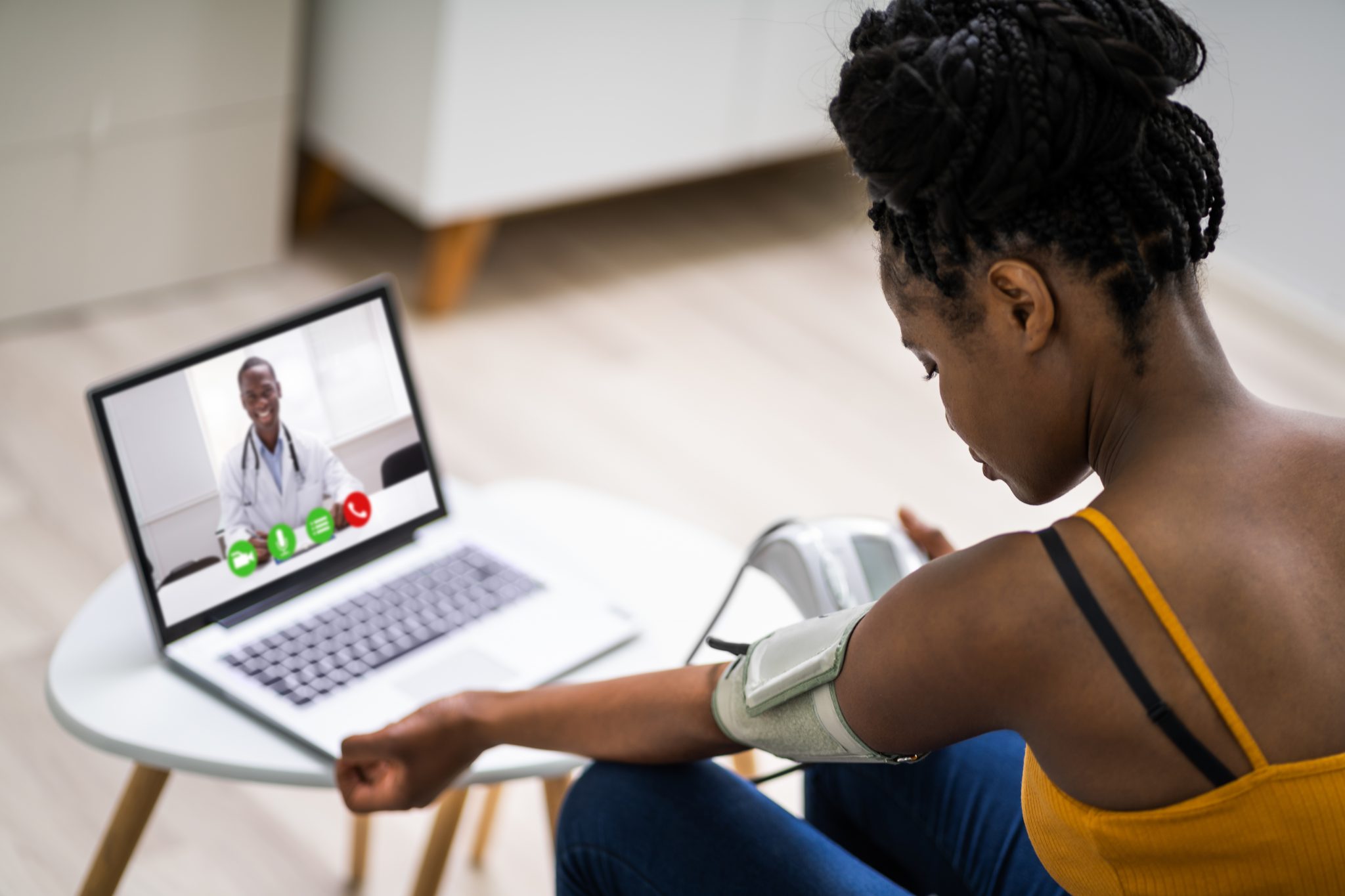 A young woman takes her own blood pressure while on a video conference with her doctor.