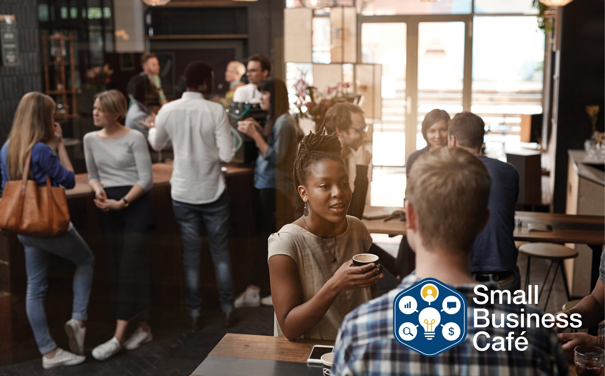 A busy cafe is full of small groups drinking coffee and talking.