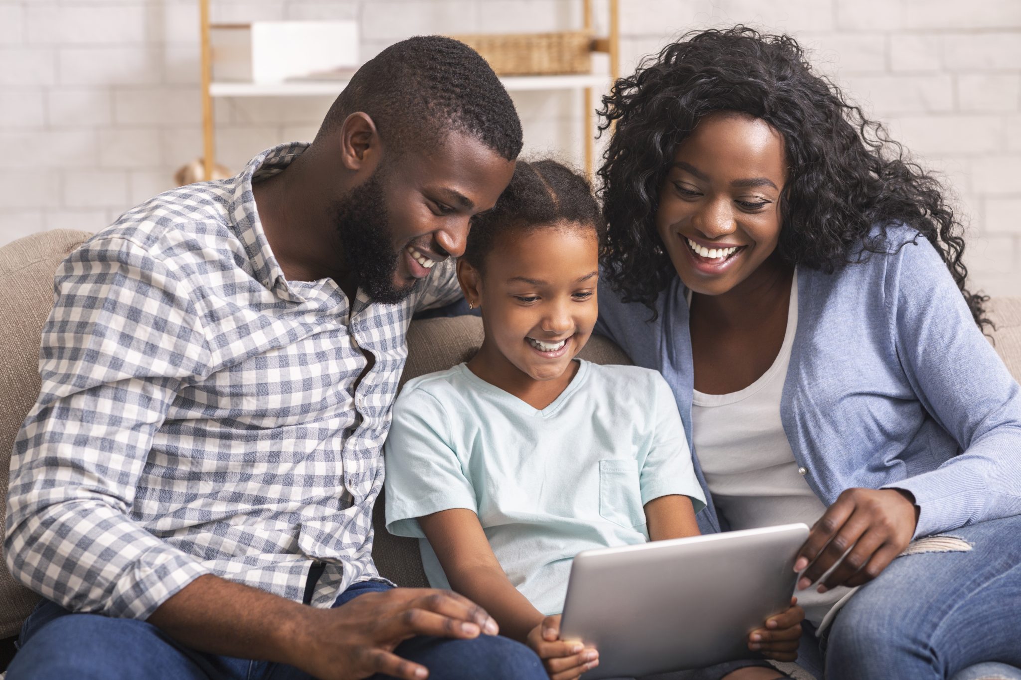 Cheerful black family using digital tablet together at home.