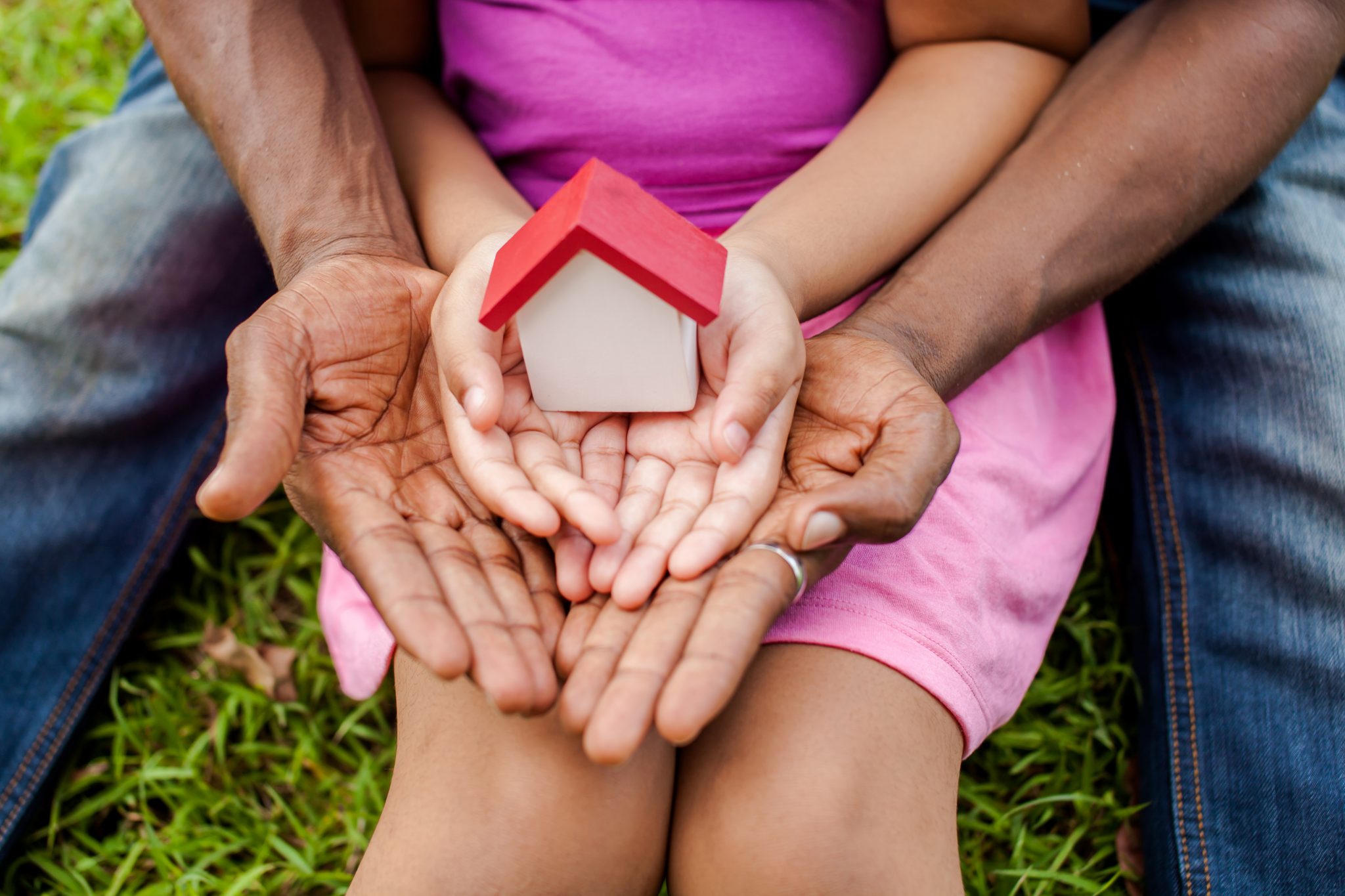 Parent and child hands hold a wooden house toy