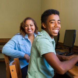 Latinx woman and African American teen sit at computers in computer lab