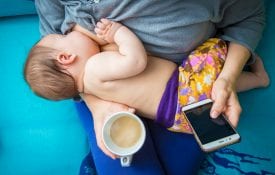 A woman breastfeeding and drinking a cup of coffee