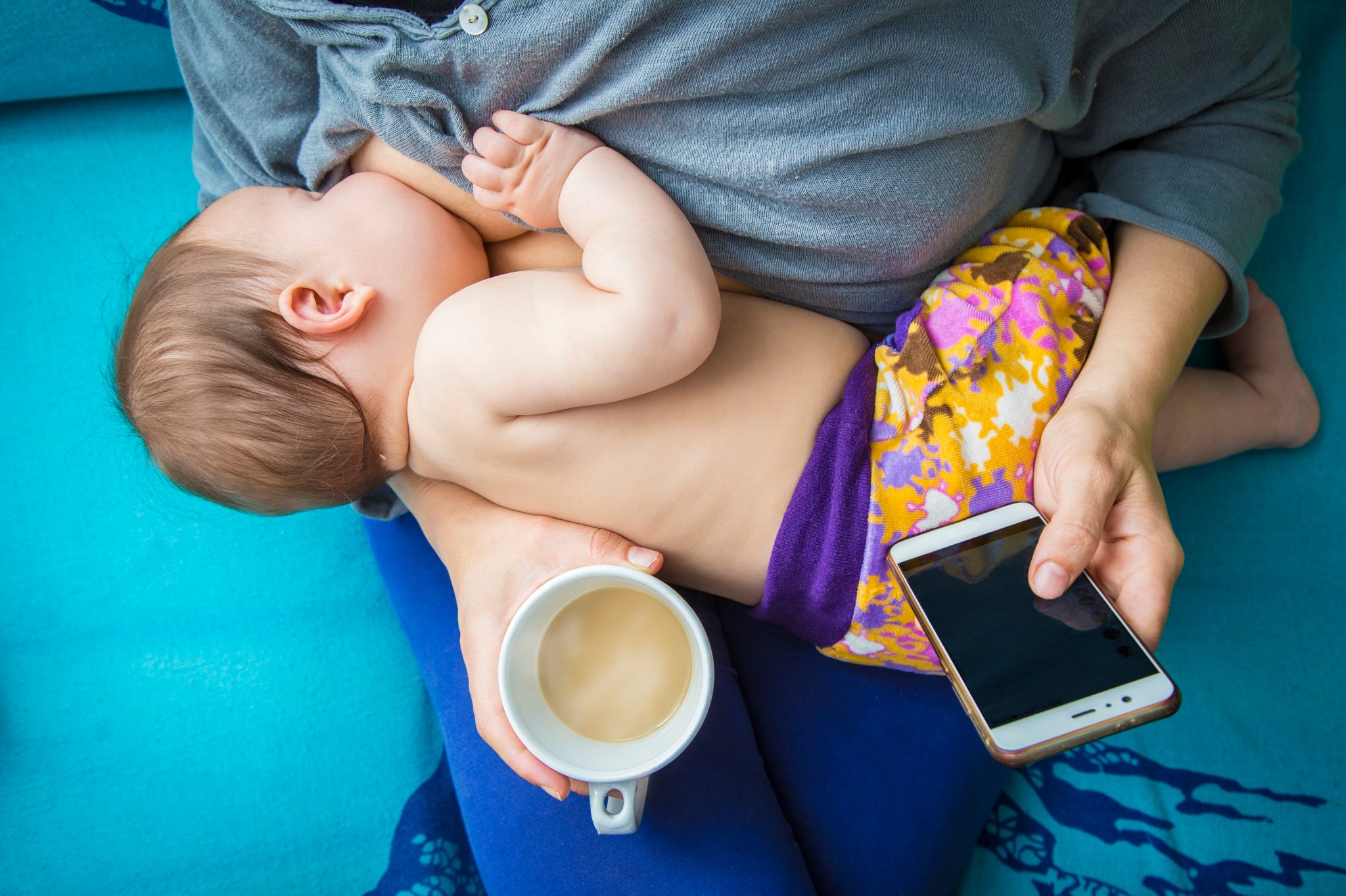 A woman breastfeeding and drinking a cup of coffee