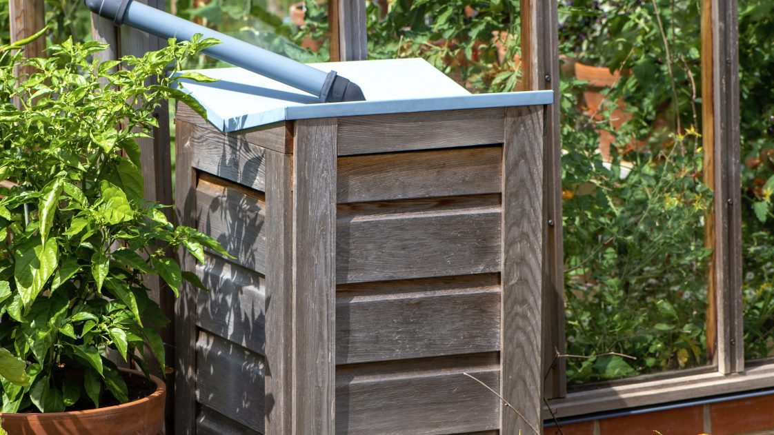 A wooden rain barrel with a plant in a pot.