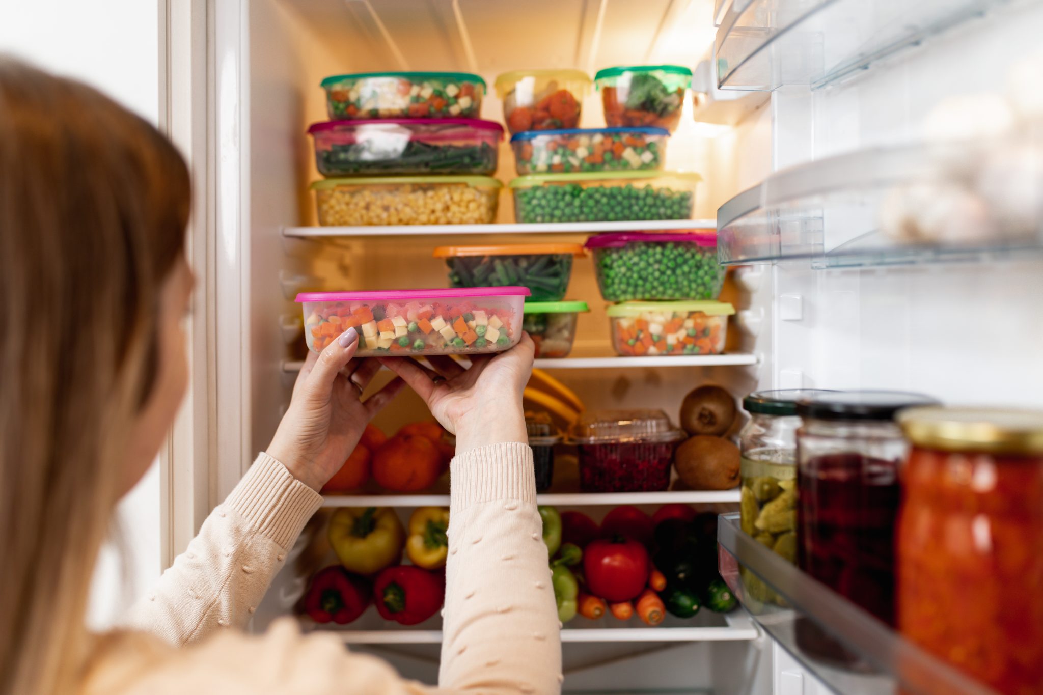 A woman storing fruits and vegetables in plastic containers.