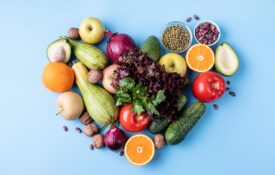 Fresh fruit and vegetables in a heart shape top view flat lay on blue background.