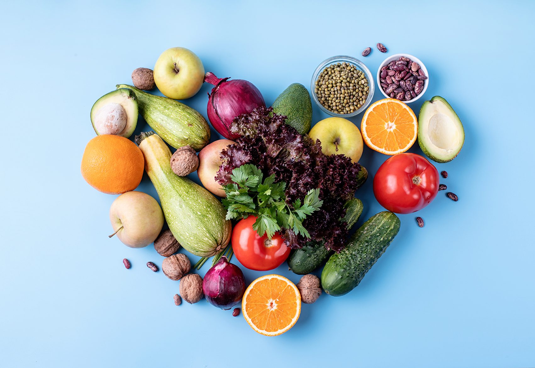 Fresh fruit and vegetables in a heart shape top view flat lay on blue background.