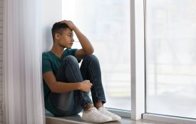 Upset teenage black boy sitting near a window