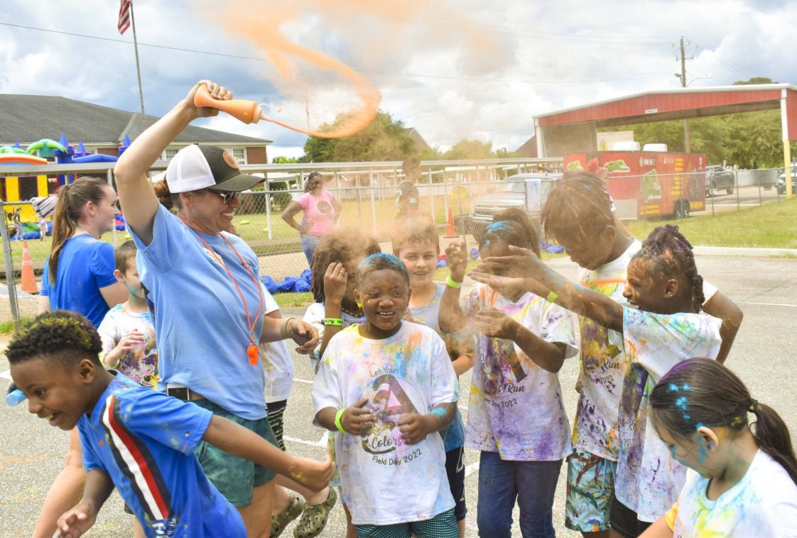 teacher pouring orange powder on students during color run
