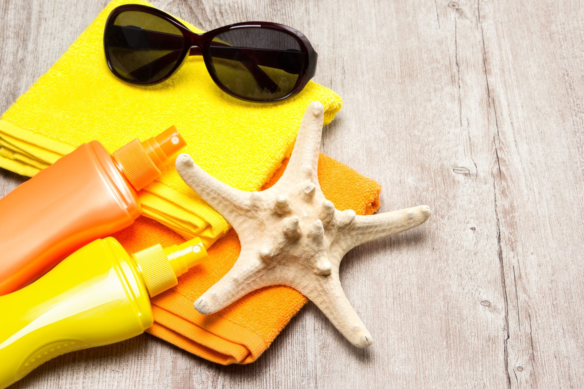 Beach towels with sunscreen, sunglasses, and a seashell.