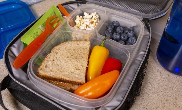 A sandwich, fruit, peppers, and popcorn packed in a lunch box