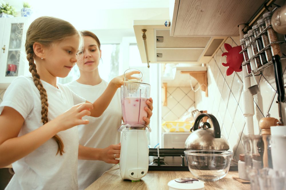 A young girl and her mother making a smoothie for breakfast.
