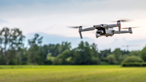 A drone flying over a field with a forest in the background.