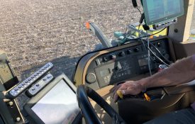 A farmer inside a tractor during harvest at sunset. You can see pieces of technology used in precision agriculture practices.
