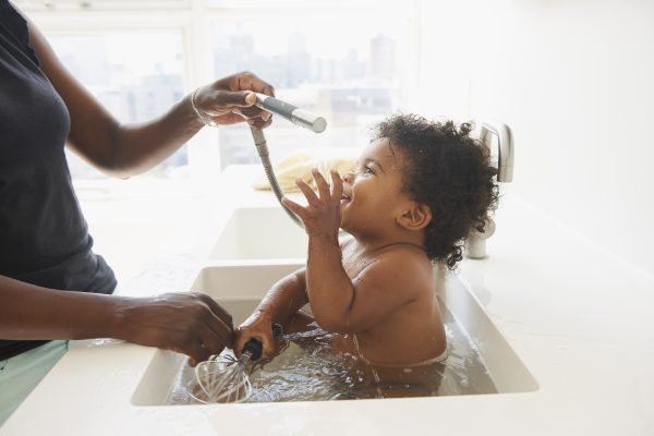 Black mother bathing baby son in sink