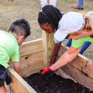 Kids and an adult preparing a raised garden bed