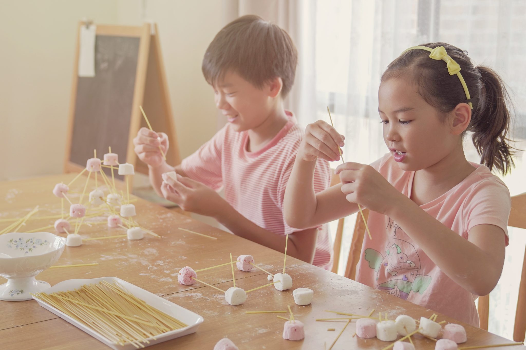 Two young Asian children building marshmallow towers