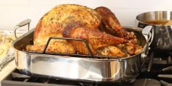 A roasted turkey sitting in a pan on the stove top.