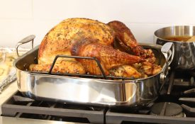 A roasted turkey sitting in a pan on the stove top.