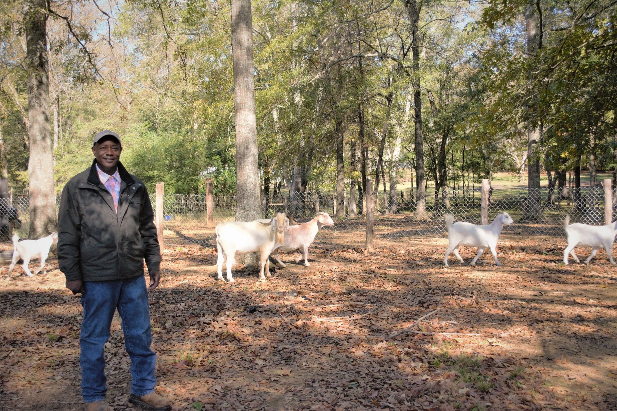 Corey Dudley in a wooded enclosure with goats behind him.