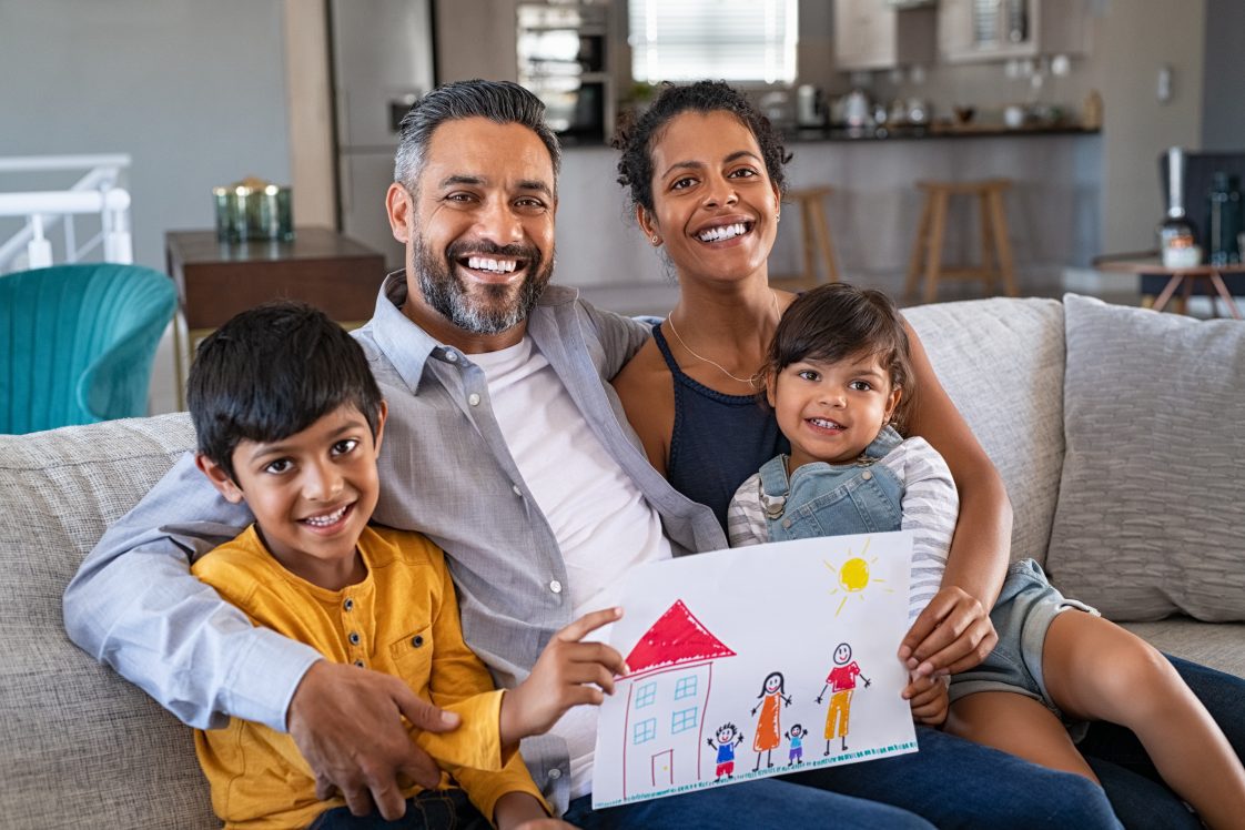 A South Asian family sitting on a couch, smiling at the camera.