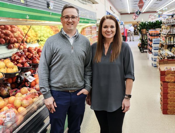 man and woman stand in front of fruit in grocery store