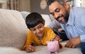 a dad helping his son put money in a piggy bank