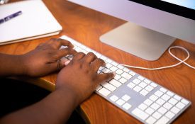 A view of a woman's hands typing on an Apple brand keyboard.