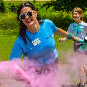 woman in blue shirt sprays pink dust during color run