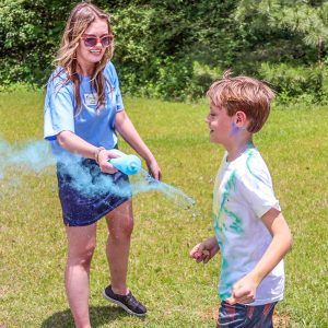 woman in blue shirt sprays kid with blue dust during color run