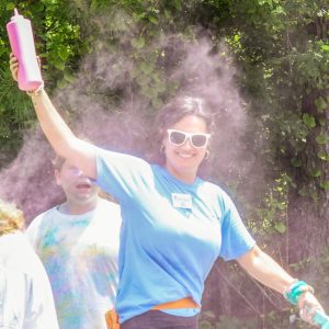 woman in blue shirt smiles in a cloud of pink dust during color run