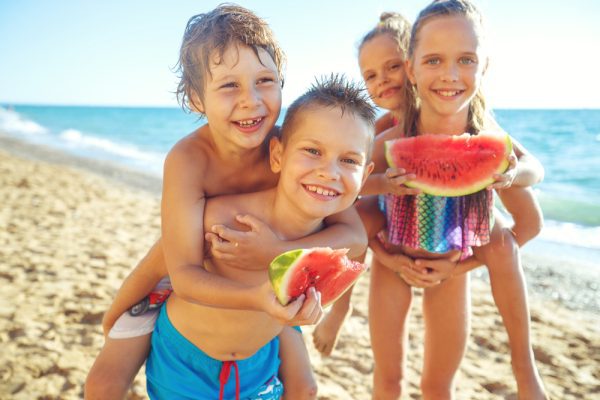 A group of children eating watermelon on the beach.