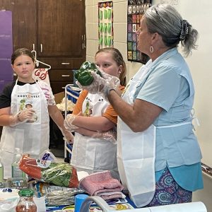 woman holding bell peppers in front of two girls during food demo