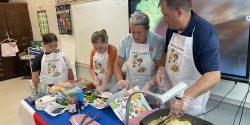 Two adults cooking next to two young girls in food demo