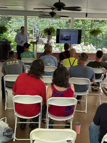 A group of people watching a presentation during an urban forestry tour.