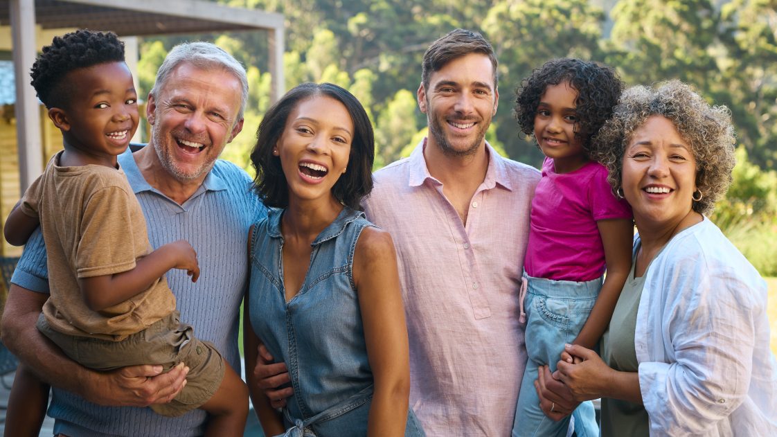 A multiracial family laughing and smiling outdoors.