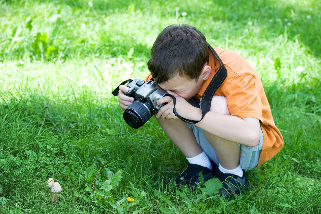 A young boy taking a picture with a camera of a mushroom.