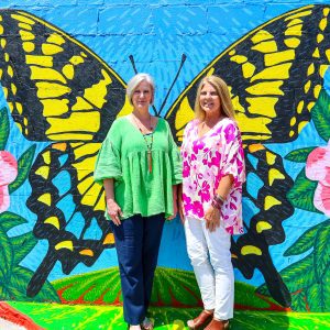 Two women posing for a photo in front of butterfly mural at the renovated terrace in Linden, Alabama.
