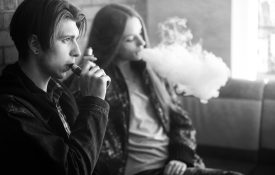 A picture of two teenagers, one male one female, vaping.