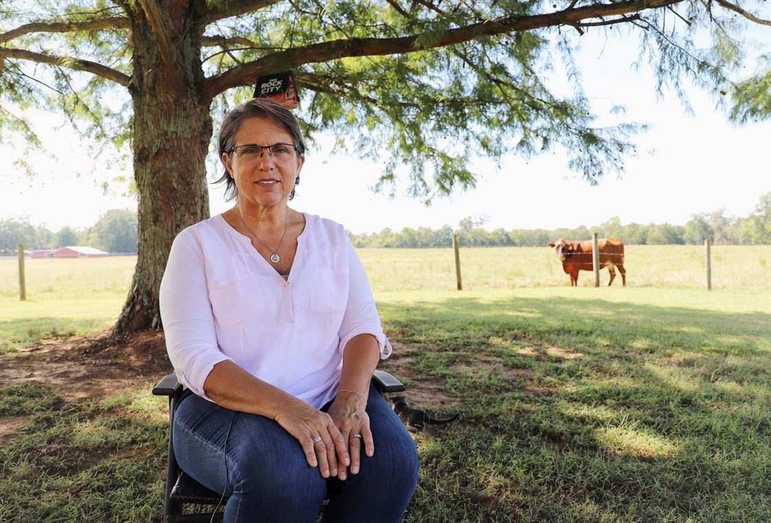 Penny Roy sitting under a tree with a pasture in the background.
