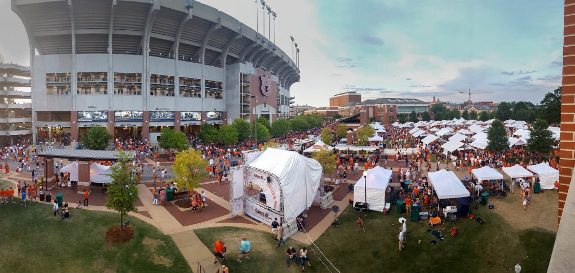 A picture of the outside of Auburn University's Jordan-Hare Stadium with people tailgating under white tents.