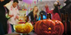 A closeup of a Halloween pumpkin on a table with chips and beer bottles.