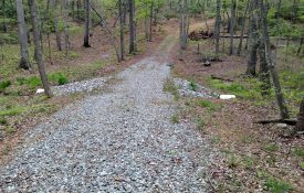A gravel road that crosses over a stream in a wooded area.