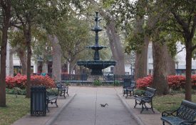The fountain in the middle of Bienville Square in Mobile, Alabama. A squirrel is playing on the sidewalk and the azaleas are blooming.